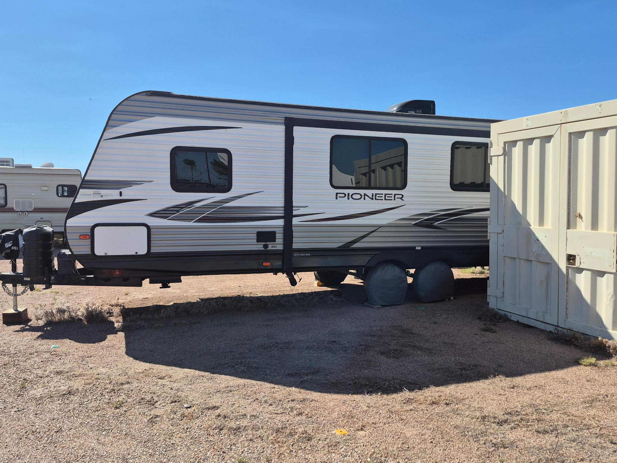 Pioneer travel trailer stored beside an on-site container